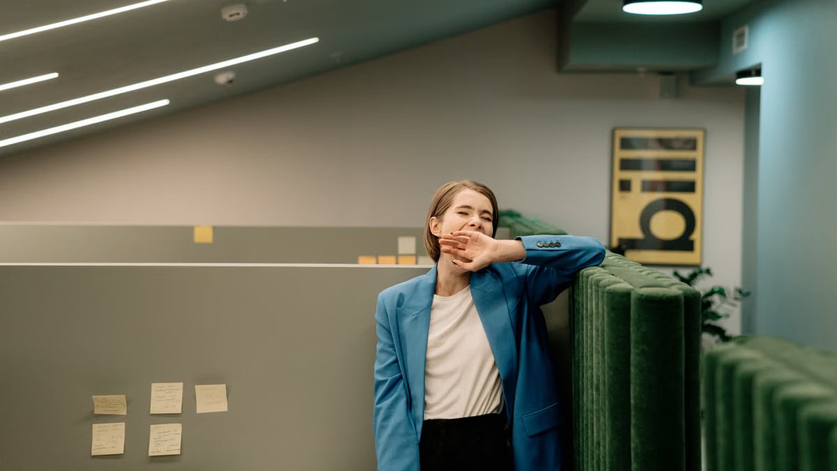Exhausted woman in blue blazer yawning during workday in corporate office.